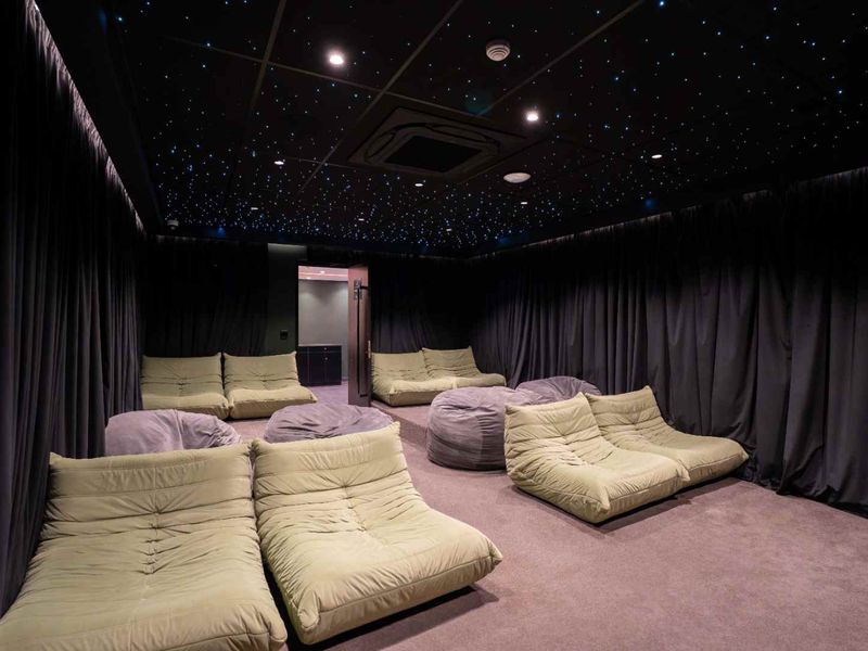 A dedicated cinema room featuring a fiber optic star ceiling, recessed lighting, integrated air conditioning, and full-height wall curtains for acoustic control.