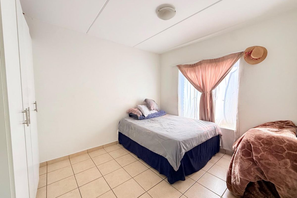 A functional bedroom featuring tiled flooring and built-in wardrobe storage, offering a simple and clean living space.