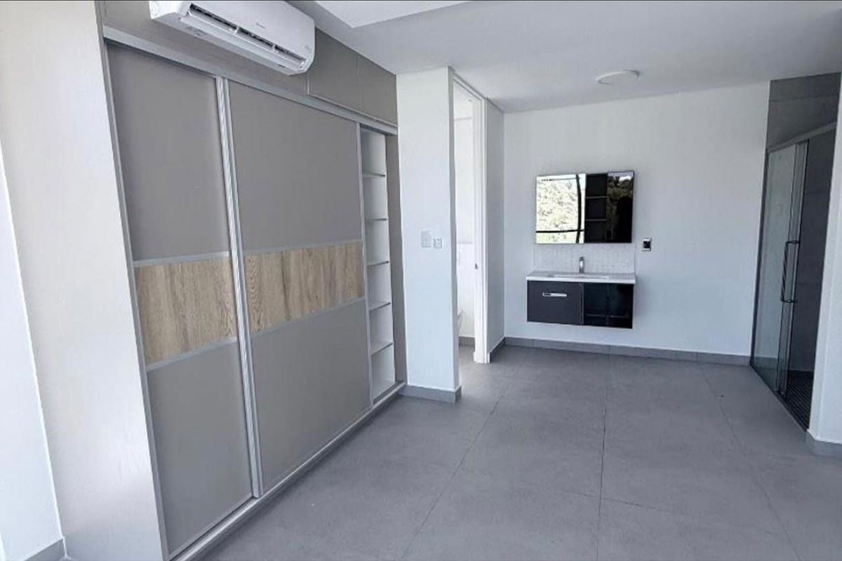Modern bedroom featuring a large built-in wardrobe, wall-mounted air conditioning, and an en-suite bathroom area with a floating vanity and glass shower.