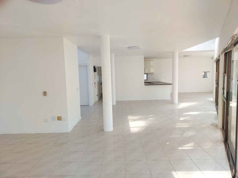 Spacious open-plan living area featuring tiled floors, structural columns, and large sliding glass doors leading to the exterior, with an integrated kitchen space.