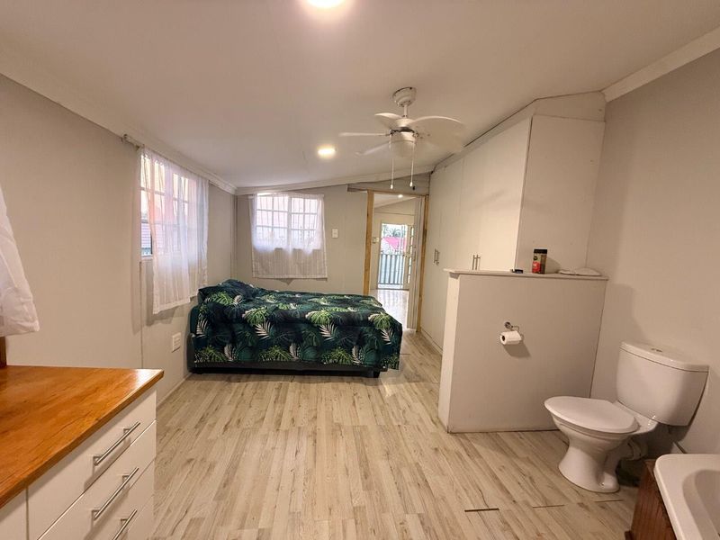 Open-plan bedroom featuring laminate flooring, built-in cupboards, and an integrated toilet area with a ceiling fan.