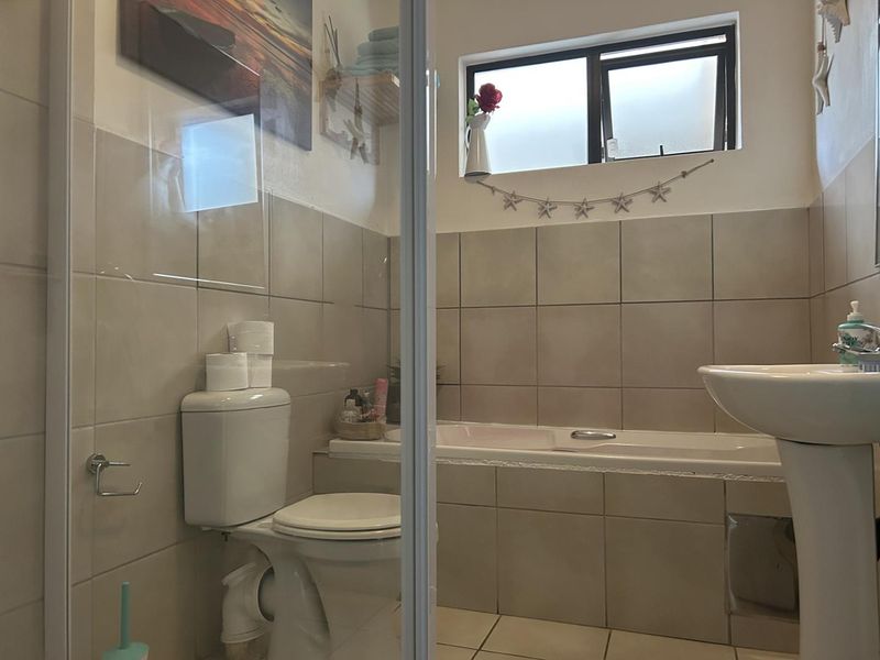 A functional bathroom featuring a pedestal basin, built-in bathtub, and toilet with neutral wall and floor tiling.