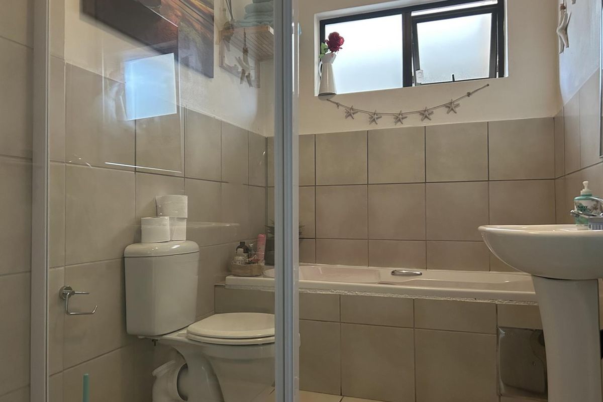 A functional bathroom featuring a pedestal basin, built-in bathtub, and toilet with neutral wall and floor tiling.