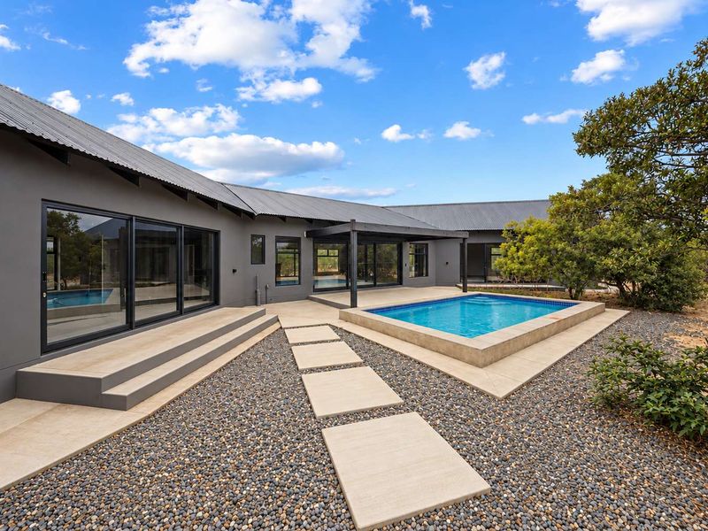 Modern outdoor living area featuring a swimming pool, concrete patio, and stepping stones, complemented by dark grey exterior walls and large sliding glass doors.