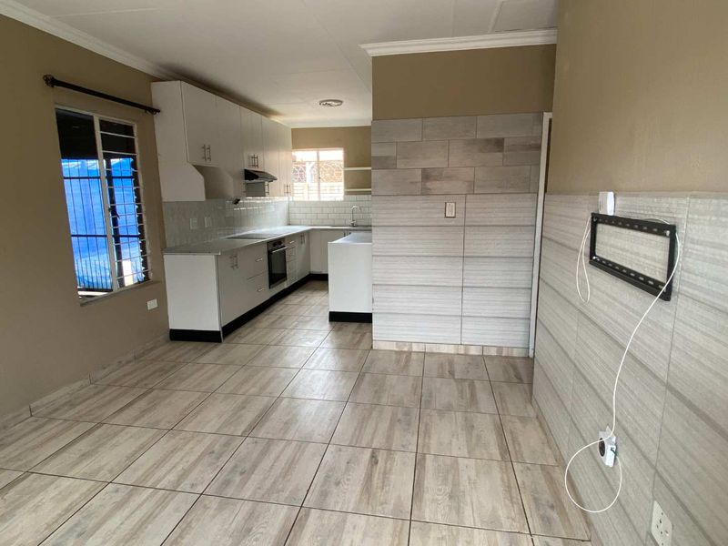 Open-plan kitchen and living area featuring modern tiled flooring, built-in cabinetry, and a tiled feature wall in a neutral townhouse setting.
