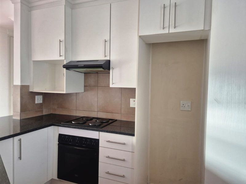 A functional kitchen featuring white cabinetry, granite countertops, a built-in oven, electric hob, and a dedicated space for a refrigerator.