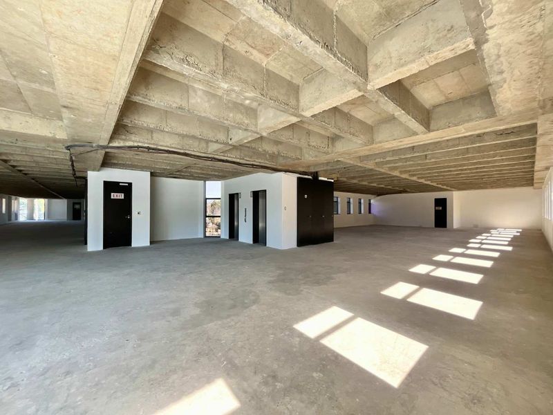 Expansive open-plan office space featuring an exposed concrete waffle slab ceiling, concrete flooring, and integrated elevator access in a shell condition.