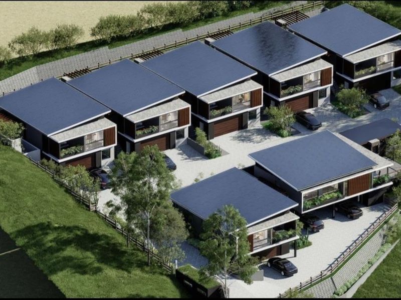 An aerial view of a modern residential housing complex featuring multiple units with solar panels, private garages, and landscaped surroundings.