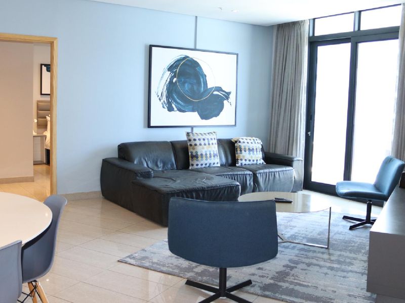 A well-maintained living room featuring tiled flooring, neutral walls, and a large sliding glass door providing natural light and access to the exterior.