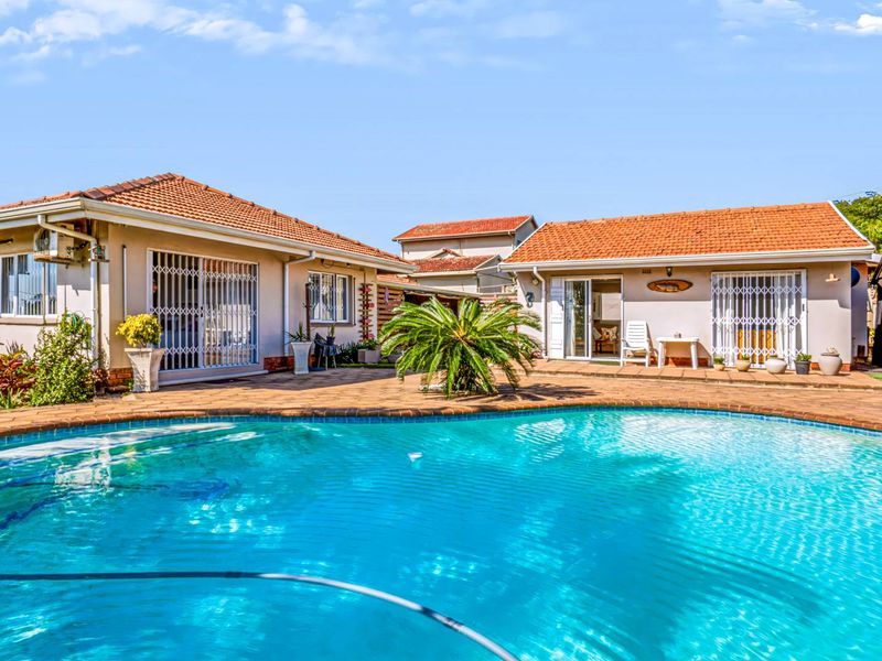 A well-maintained outdoor pool area featuring a paved patio, tiled roof structures, and secure access points to the main residence.