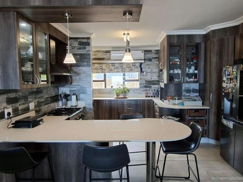 Modern kitchen featuring dark wood cabinetry, stone countertops, a breakfast bar, and integrated appliances, offering a functional and stylish cooking and dining space.