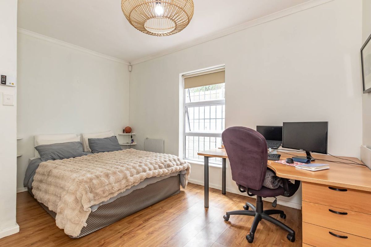 A functional bedroom featuring laminate flooring, a window with security bars, and a neutral color palette, suitable for use as a bedroom or home office.