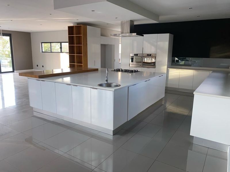 Modern, spacious kitchen featuring a large central island with a gas hob, built-in ovens, sleek white cabinetry, and polished tiled flooring.