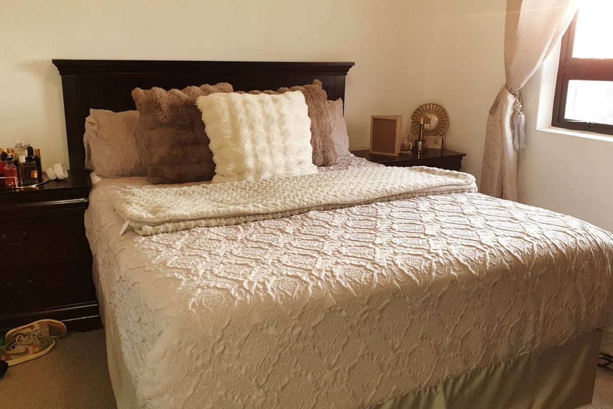A cozy bedroom featuring neutral wall tones, carpeted flooring, and a window allowing natural light into the space.