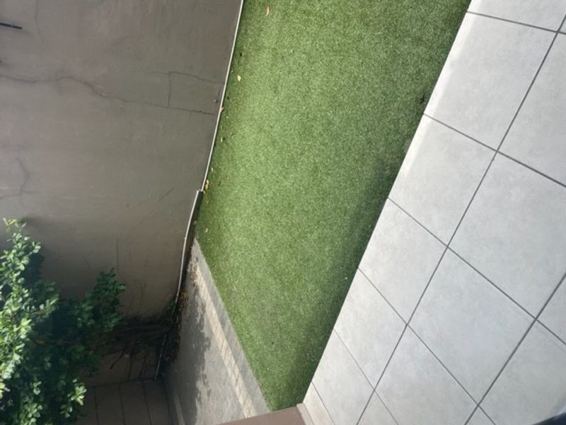 A small outdoor patio area featuring artificial grass and tiled flooring, bordered by a boundary wall.