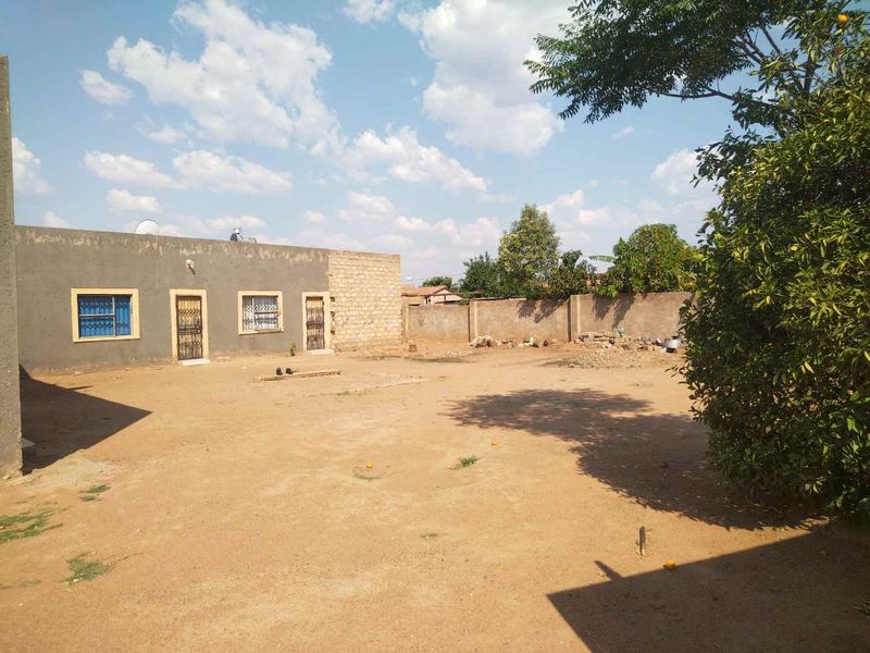 Spacious rear yard area featuring a perimeter wall and an unfinished exterior building facade with security-barred windows.
