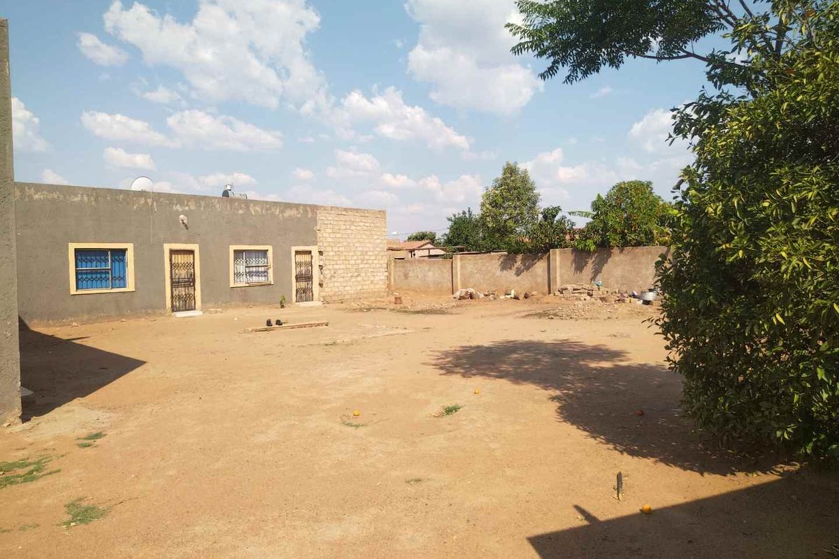 Spacious rear yard area featuring a perimeter wall and an unfinished exterior building facade with security-barred windows.