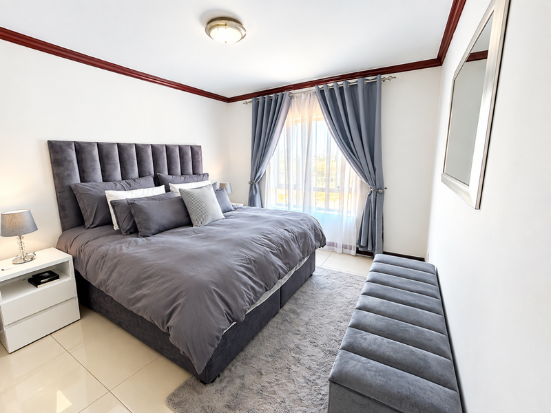 A well-maintained bedroom featuring tiled flooring, crown molding, and a large window with curtains, providing a bright and comfortable living space.