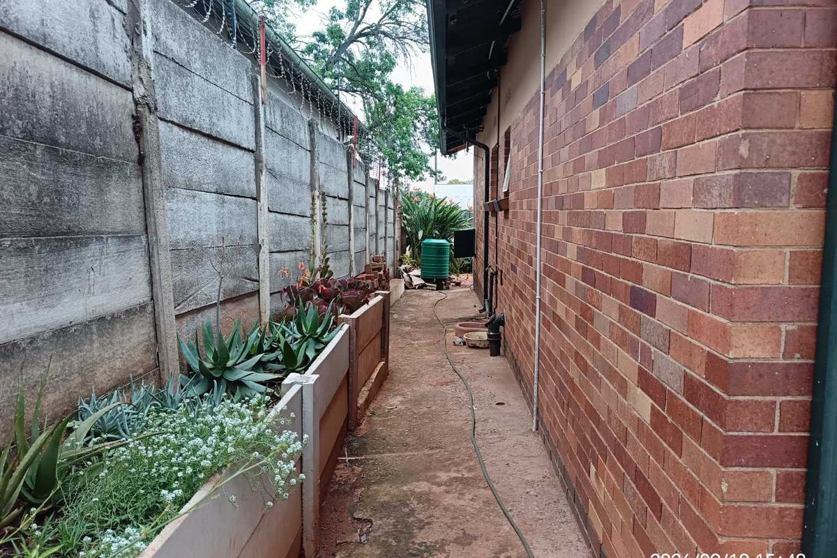 A narrow side passage featuring a brick exterior wall, a precast concrete boundary wall with security razor wire, and a water tank.