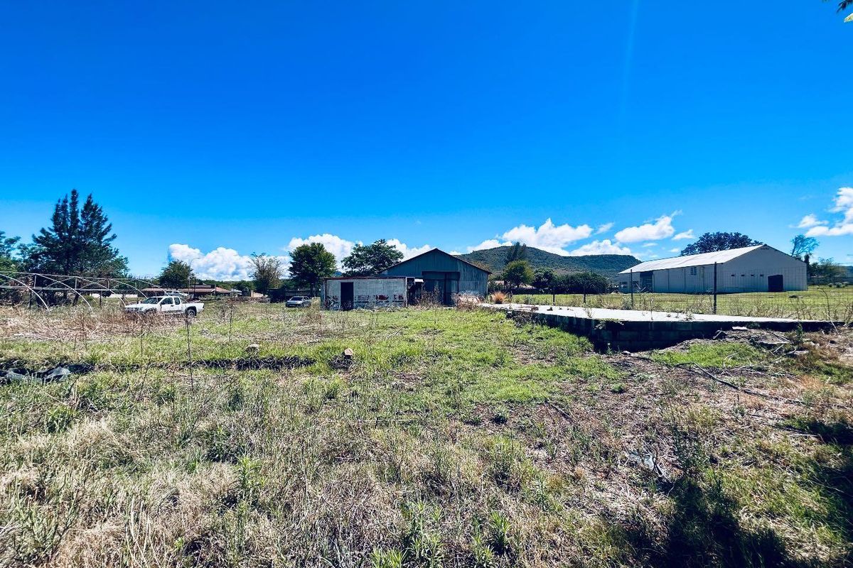 A vacant residential plot featuring overgrown grass, a dilapidated outbuilding, and an existing concrete foundation slab with mountain views in the background.