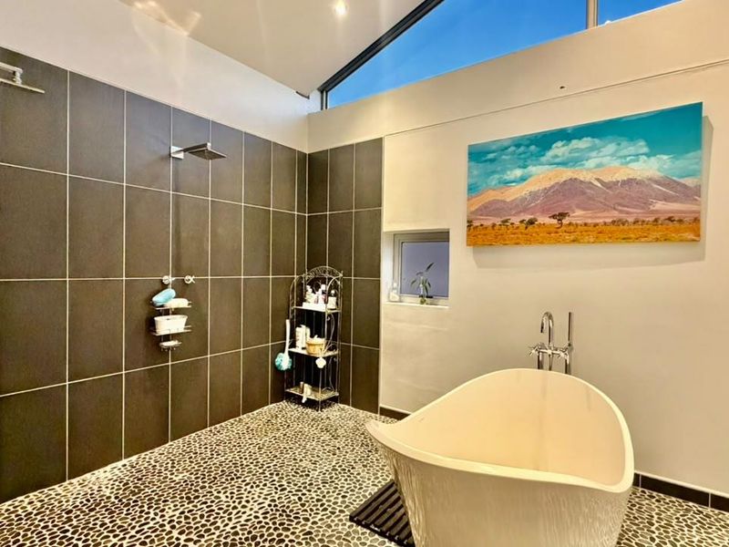 Modern bathroom featuring a spacious walk-in shower with dark tiling, pebble flooring, and a contemporary freestanding bathtub under clerestory windows.