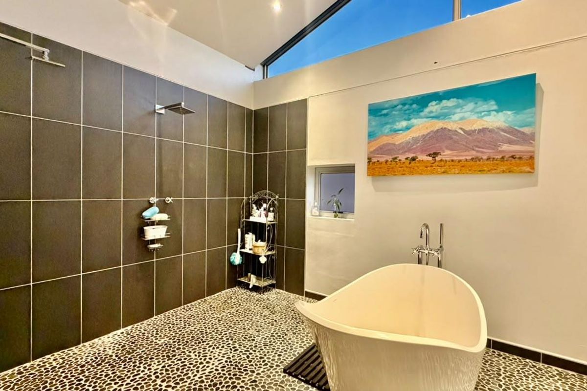 Modern bathroom featuring a spacious walk-in shower with dark tiling, pebble flooring, and a contemporary freestanding bathtub under clerestory windows.