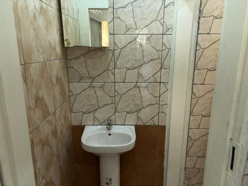A compact bathroom featuring a pedestal washbasin and decorative ceramic wall tiling, currently in need of cosmetic updates.