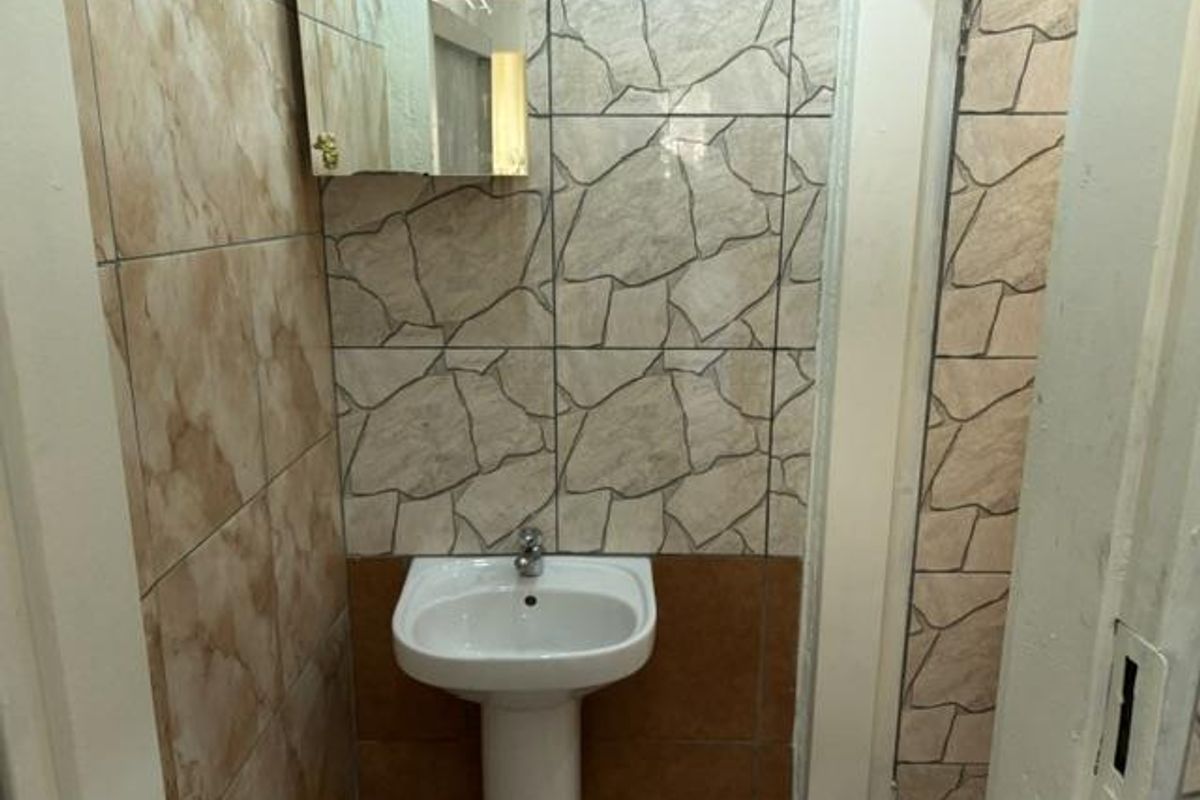 A compact bathroom featuring a pedestal washbasin and decorative ceramic wall tiling, currently in need of cosmetic updates.