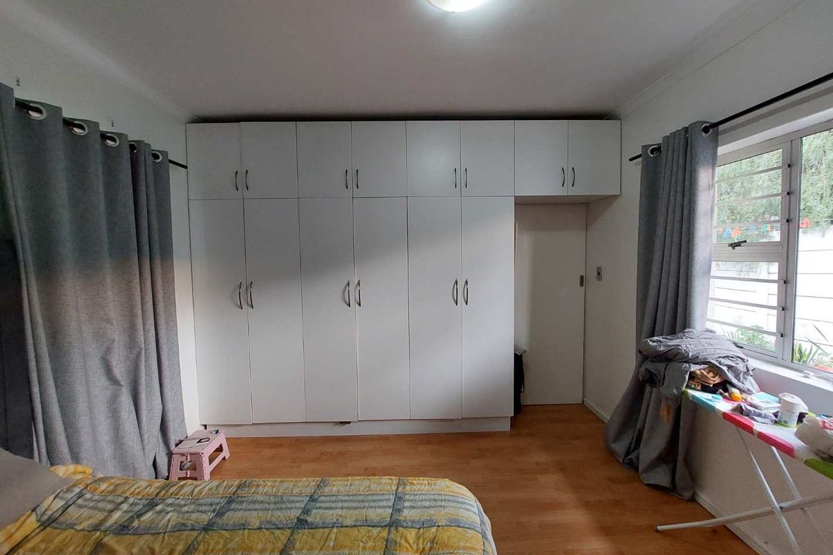 A bedroom featuring extensive floor-to-ceiling built-in cabinetry with white doors, providing ample storage space, complemented by laminate flooring and natural light.