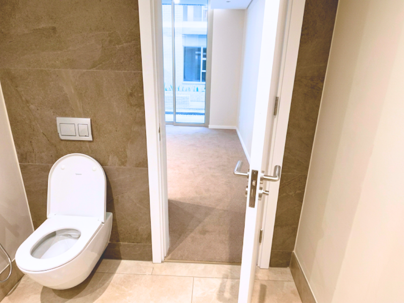 A modern, minimalist bathroom featuring a wall-mounted toilet with a bidet spray, complemented by neutral-toned wall and floor tiling.