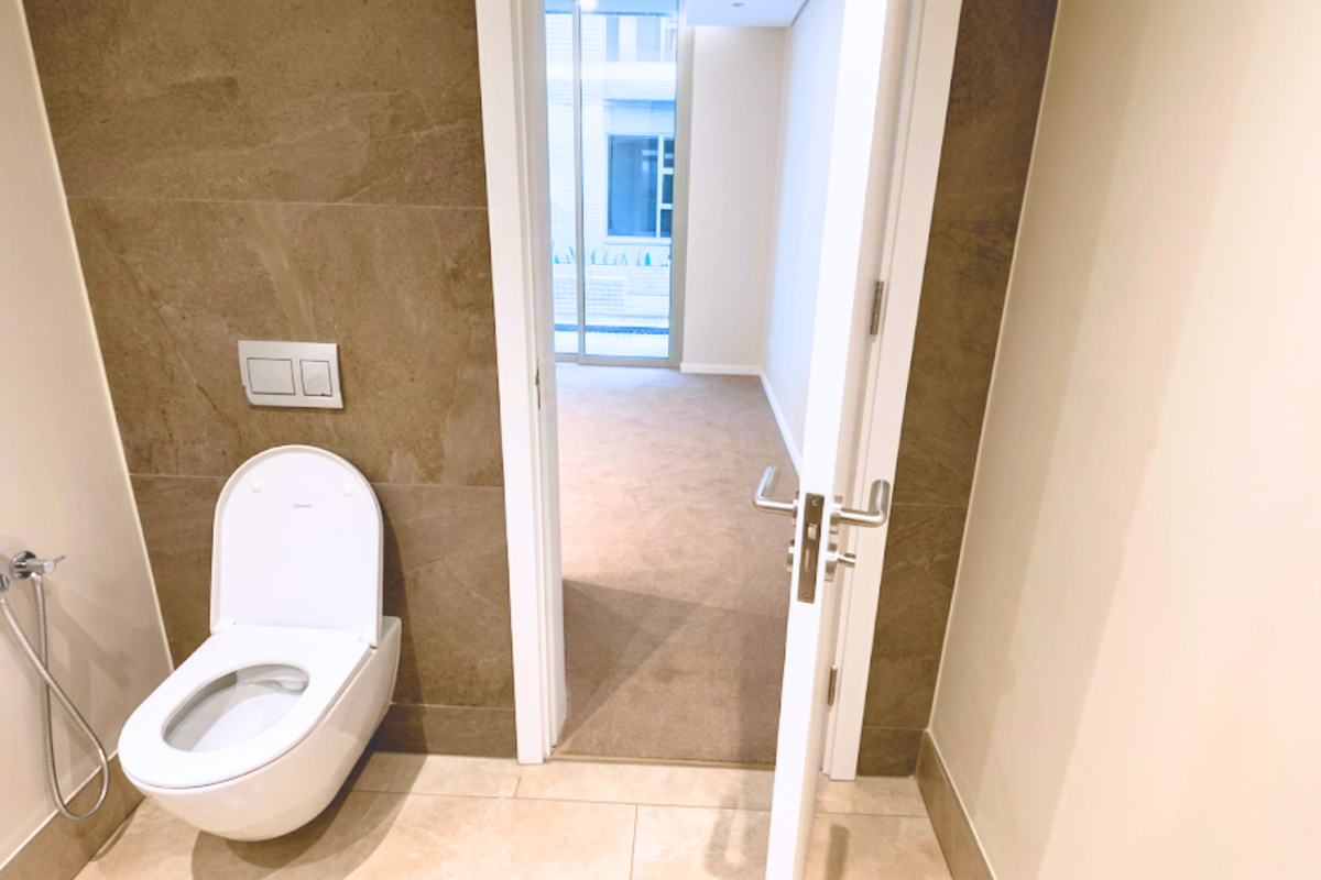 A modern, minimalist bathroom featuring a wall-mounted toilet with a bidet spray, complemented by neutral-toned wall and floor tiling.