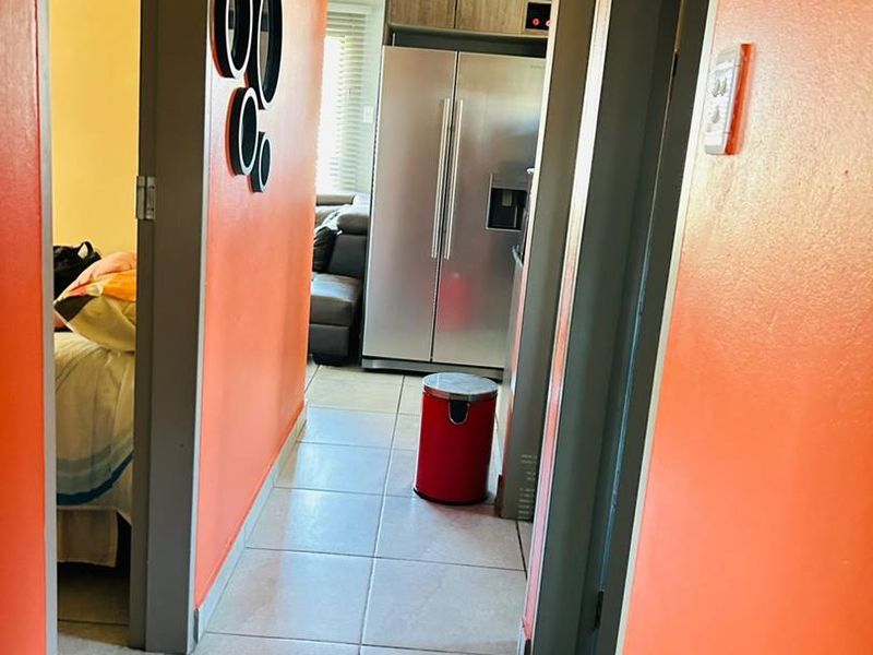A view through a hallway with tiled flooring, leading towards a kitchen area with built-in cabinetry and a stainless steel refrigerator.