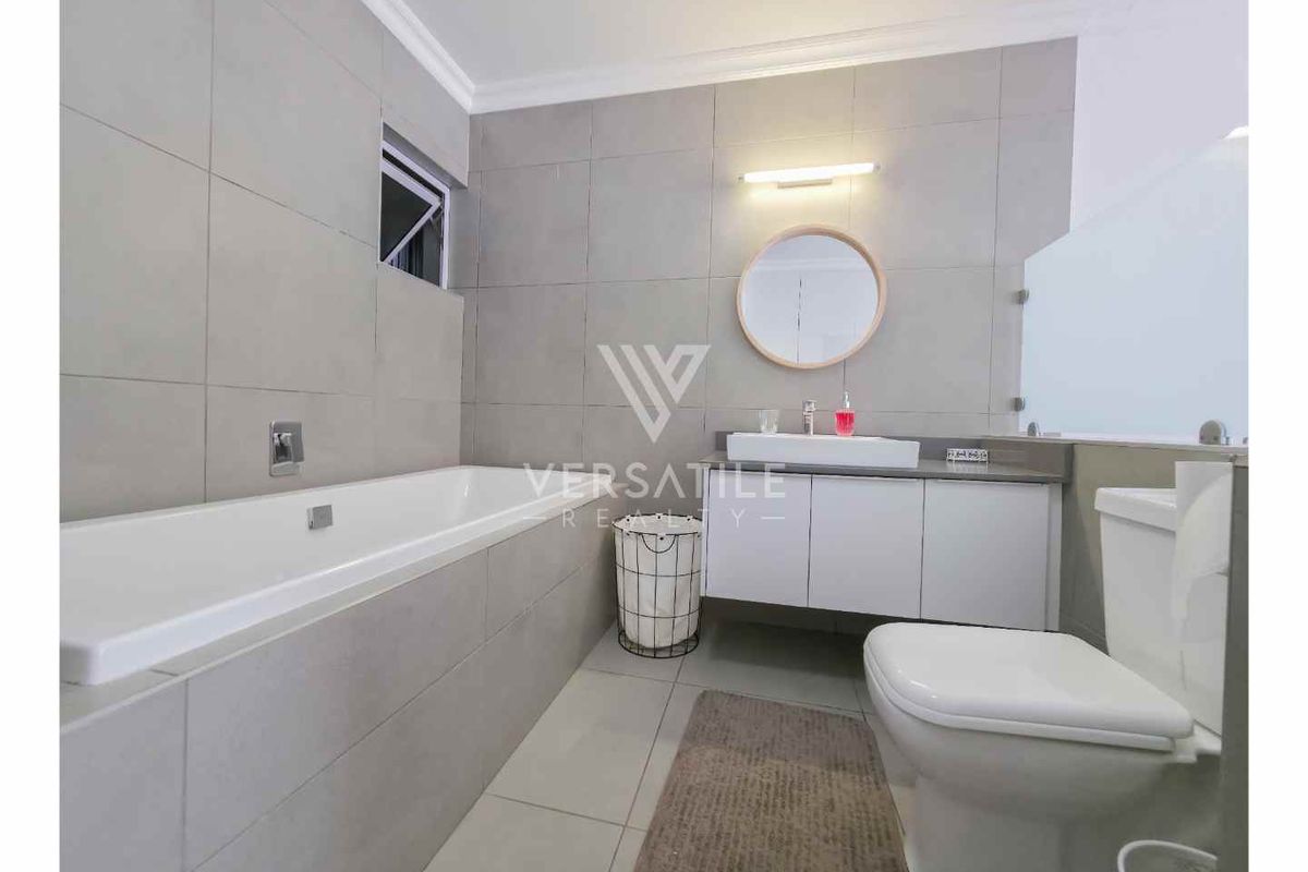 Modern bathroom featuring large format grey wall tiles, a built-in bathtub, a floating vanity with a vessel sink, and a wall-mounted toilet.
