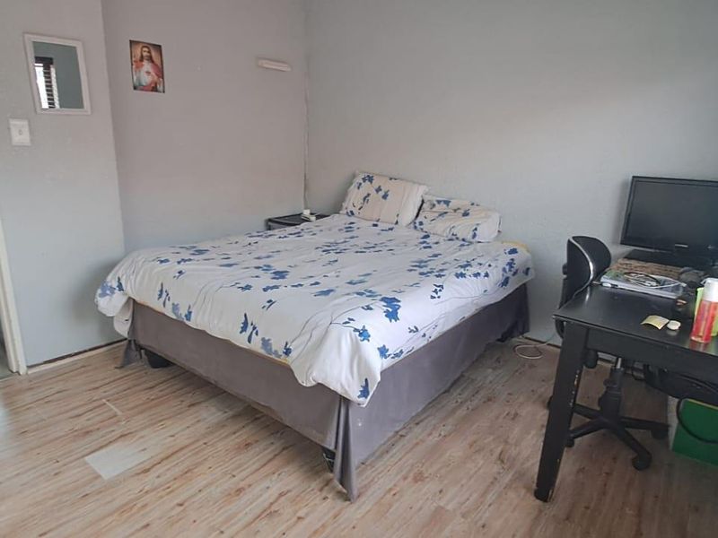 A bedroom featuring laminate flooring and venetian blinds, showing signs of wear and requiring cosmetic updates.
