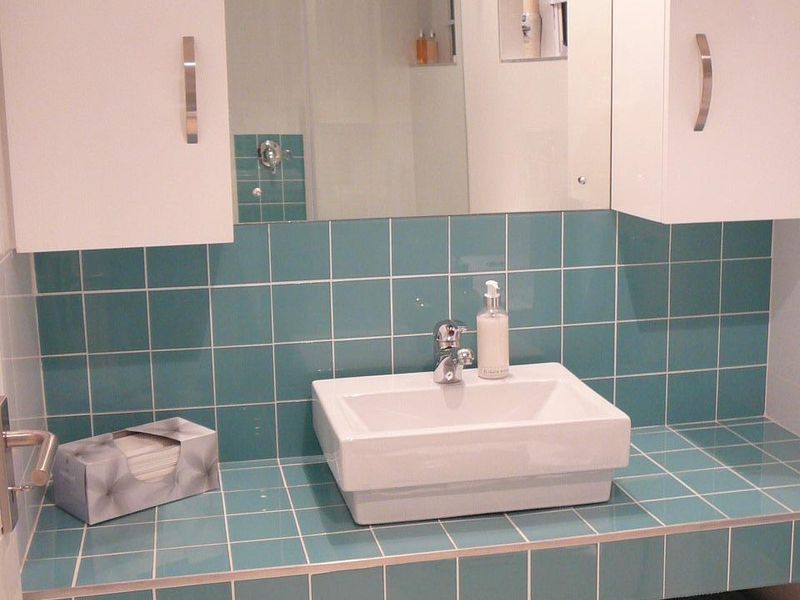 A bathroom vanity featuring a modern vessel sink, teal square tiling, and built-in white cabinetry with integrated storage.