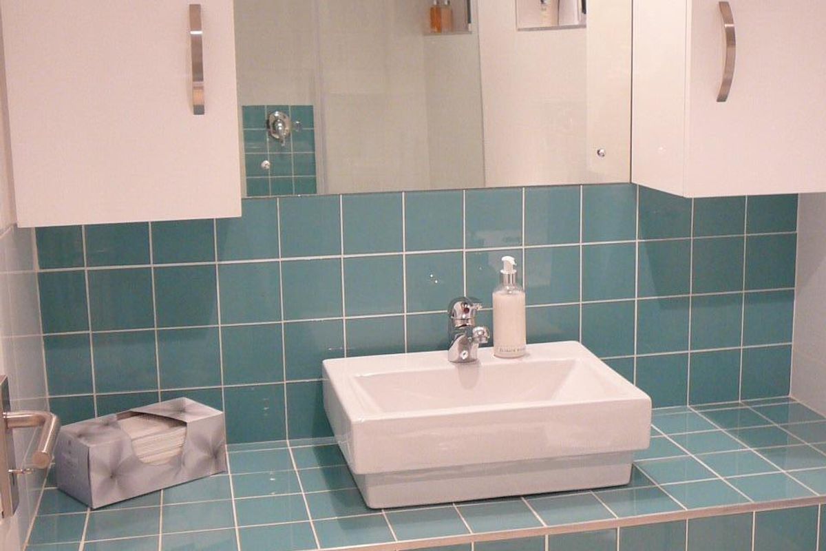 A bathroom vanity featuring a modern vessel sink, teal square tiling, and built-in white cabinetry with integrated storage.