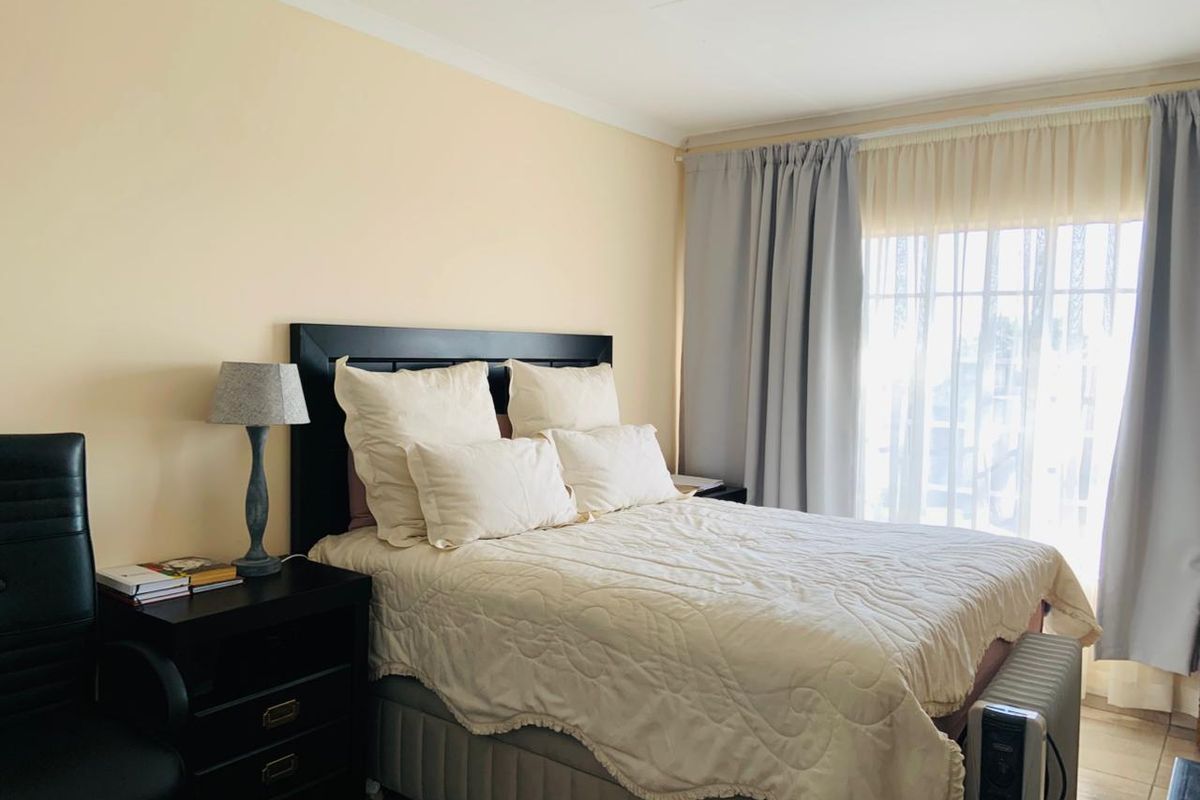 A well-lit bedroom featuring neutral wall tones, tiled flooring, and large windows with curtain tracks, providing a comfortable and functional living space.