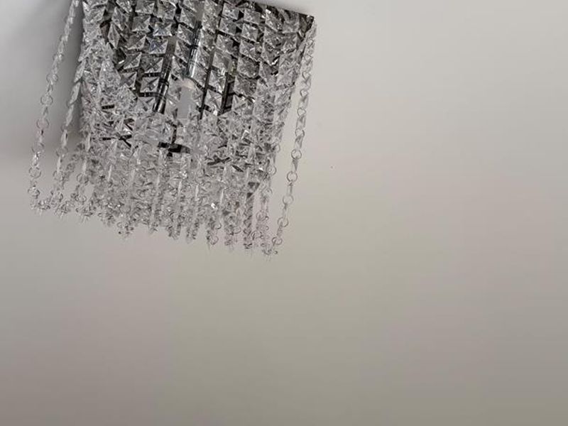 A close-up view of a decorative crystal chandelier mounted on a plain white ceiling.