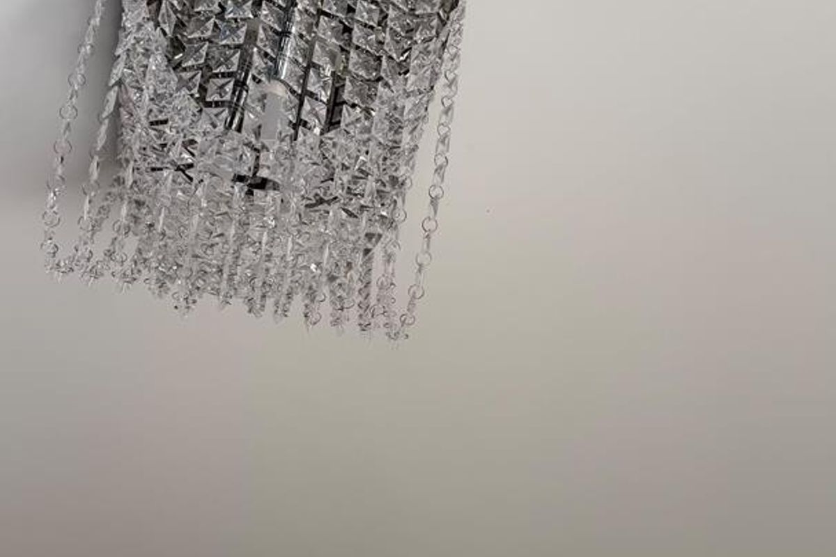 A close-up view of a decorative crystal chandelier mounted on a plain white ceiling.