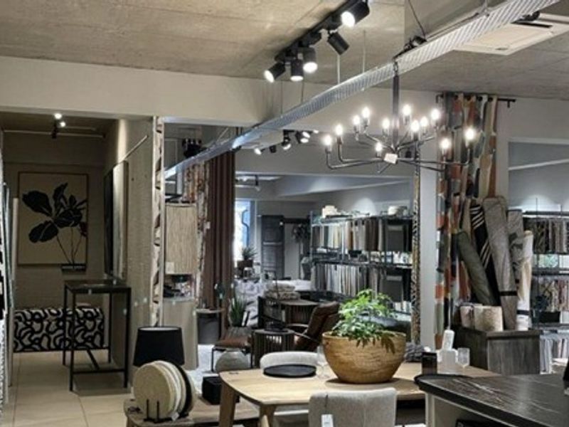 Spacious open-plan commercial showroom featuring exposed concrete ceilings, modern track lighting, a decorative chandelier, and durable tiled flooring.