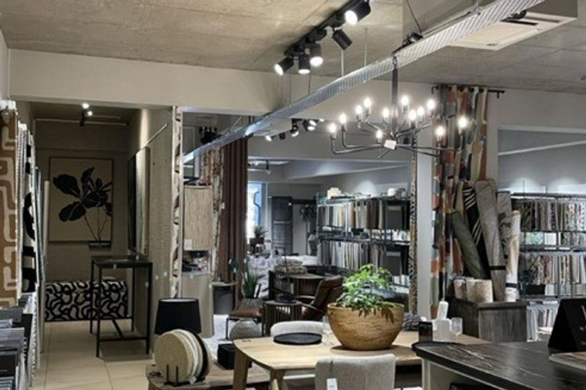 Spacious open-plan commercial showroom featuring exposed concrete ceilings, modern track lighting, a decorative chandelier, and durable tiled flooring.