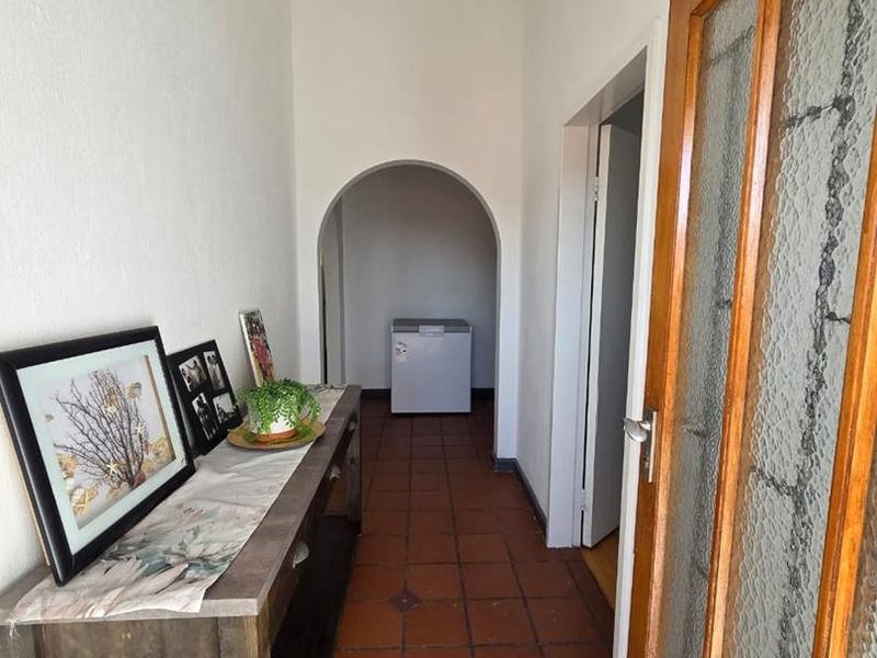 A bright hallway featuring terracotta floor tiles, an arched transition, and a classic timber-framed glass door leading to adjacent living spaces.