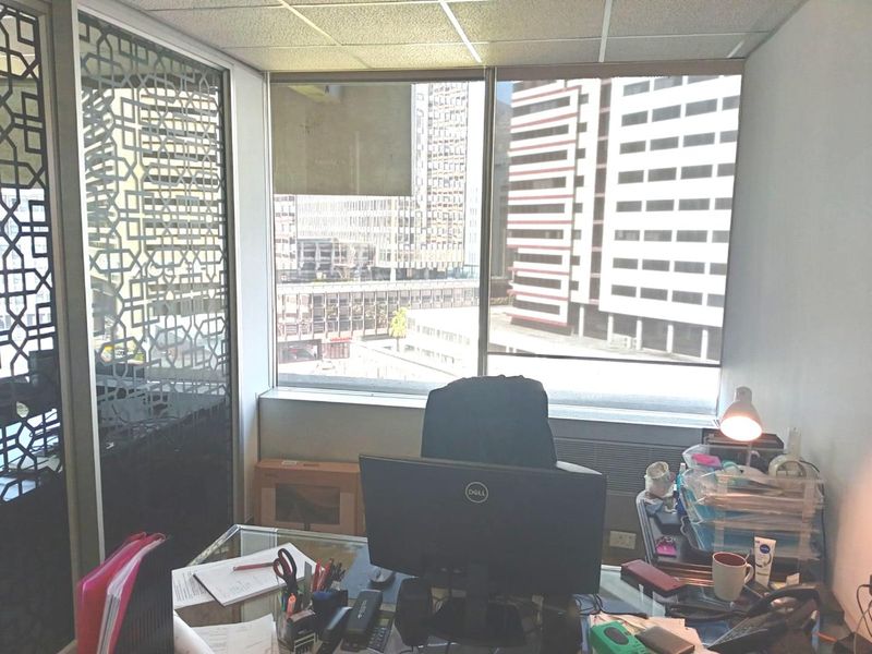 A functional office space featuring a decorative metal partition, large windows with city views, and a suspended ceiling.
