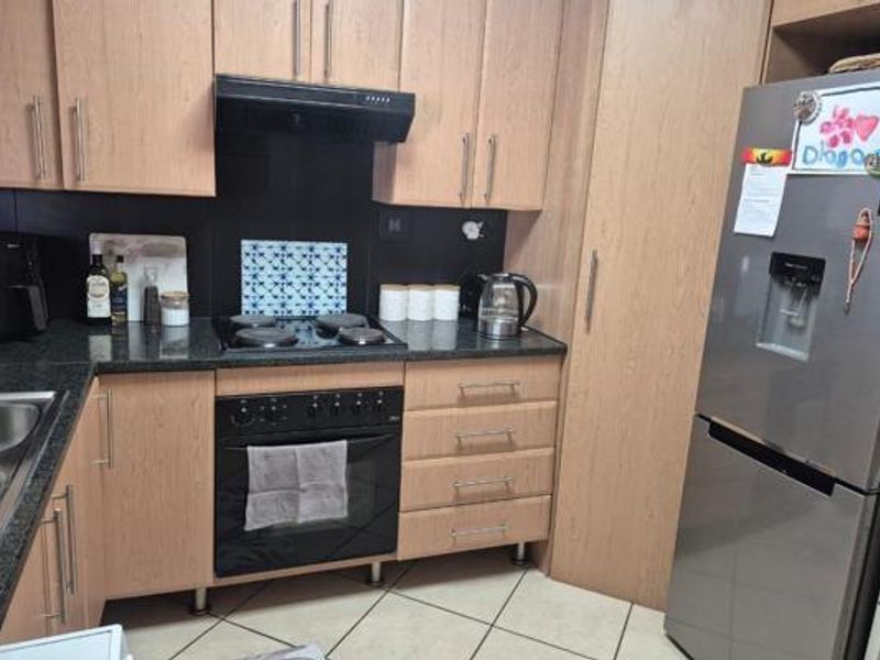 A functional kitchen featuring laminate cabinetry, granite countertops, a built-in oven with electric hob, extractor fan, and tiled flooring.