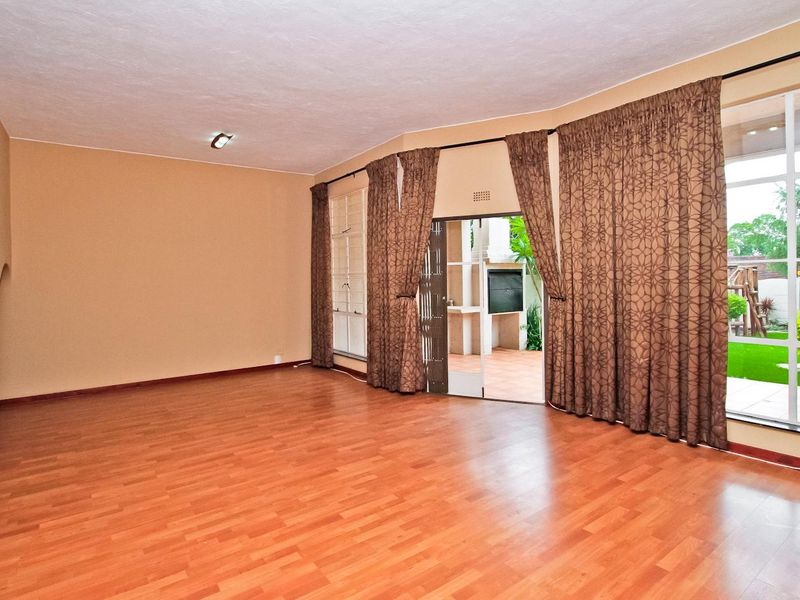 Spacious, empty living room featuring laminate flooring, large windows, and direct access to an outdoor patio area.