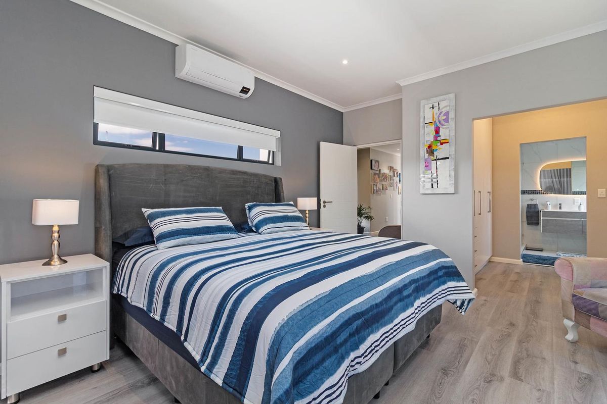 A well-maintained bedroom featuring light wood-look flooring, a wall-mounted air conditioning unit, and an adjoining en-suite bathroom with modern finishes.