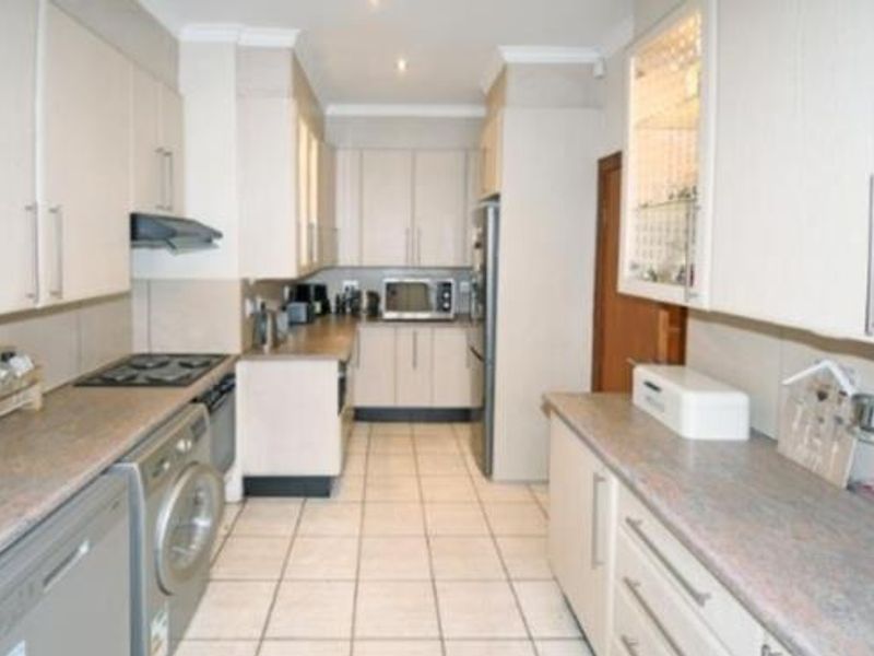 A functional galley-style kitchen featuring neutral cabinetry, laminate countertops, tiled flooring, and integrated appliances including a hob, oven, and extractor fan.