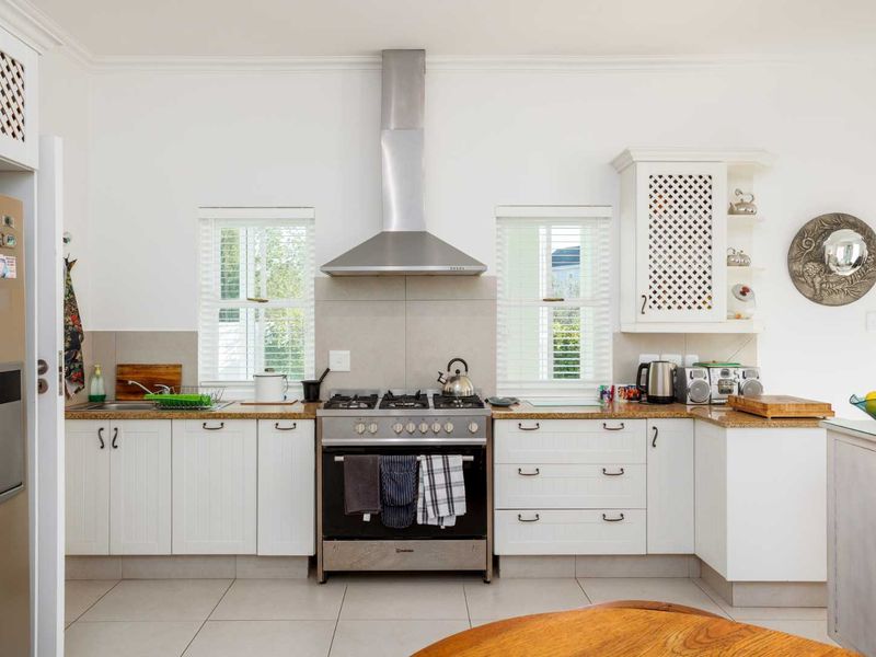 A well-maintained kitchen featuring white cabinetry, granite countertops, a stainless steel gas stove with extractor fan, and tiled flooring.