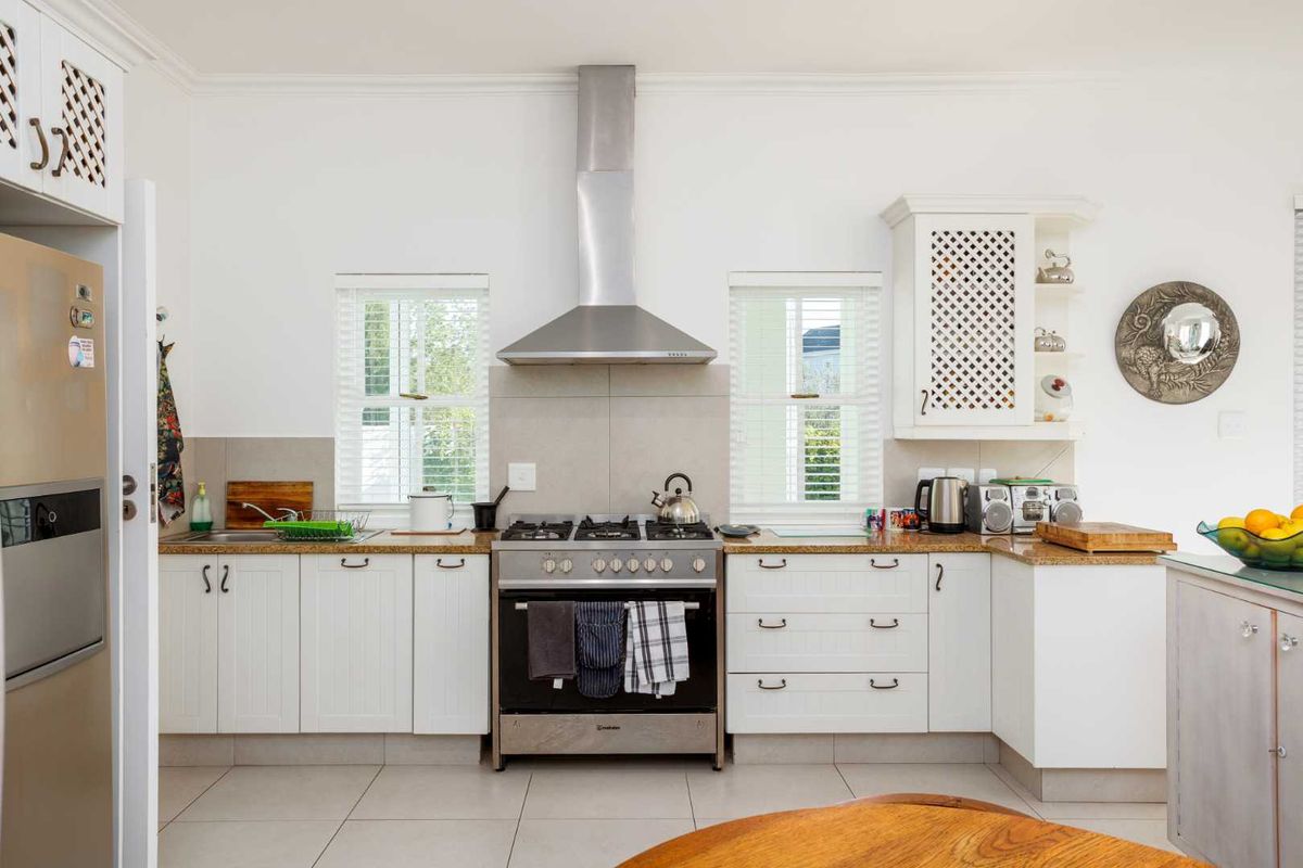 A well-maintained kitchen featuring white cabinetry, granite countertops, a stainless steel gas stove with extractor fan, and tiled flooring.