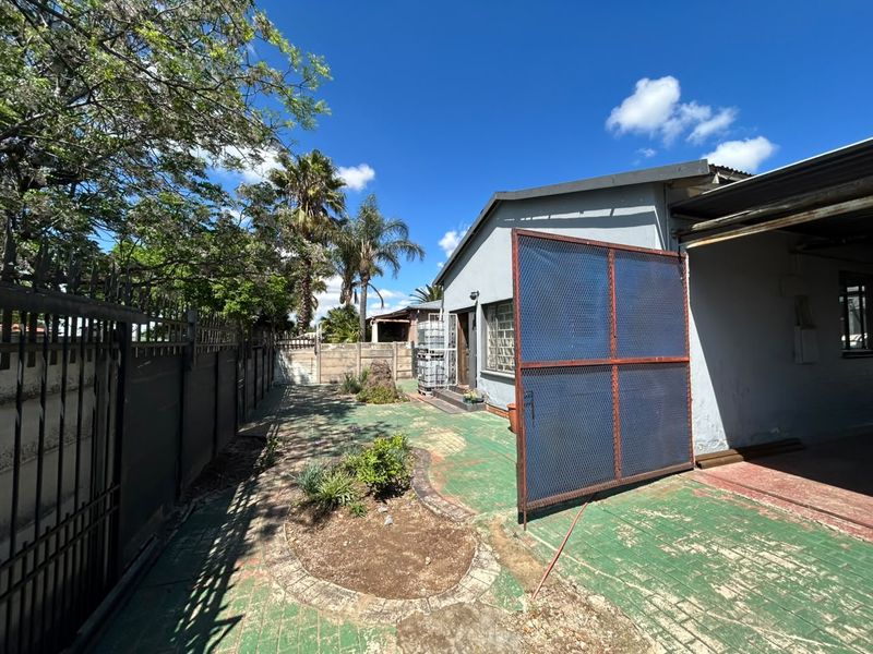 Rear exterior area featuring a paved patio, perimeter wall with security spikes, and a large metal security gate.